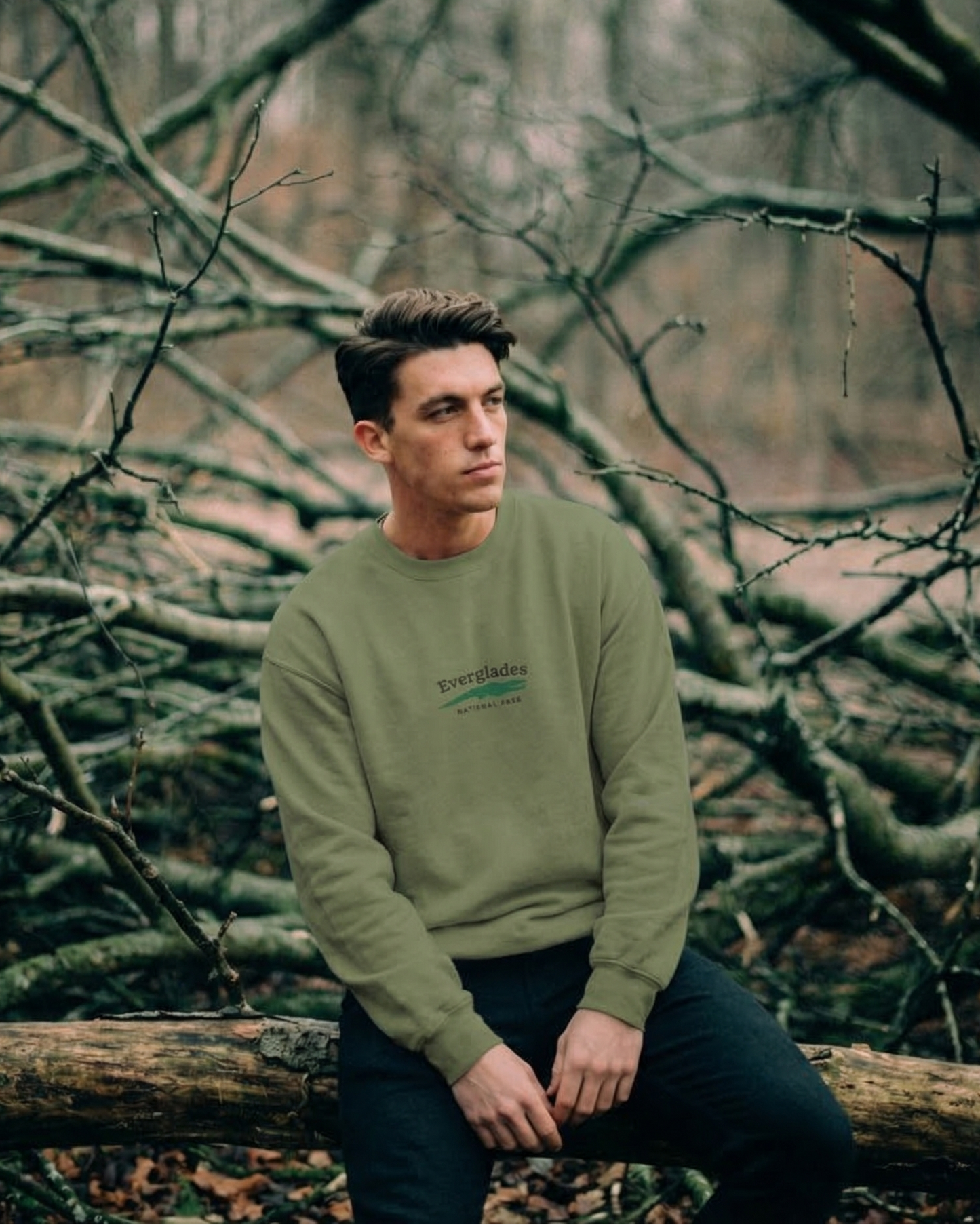 Man sitting on a log in a forest with bare trees
