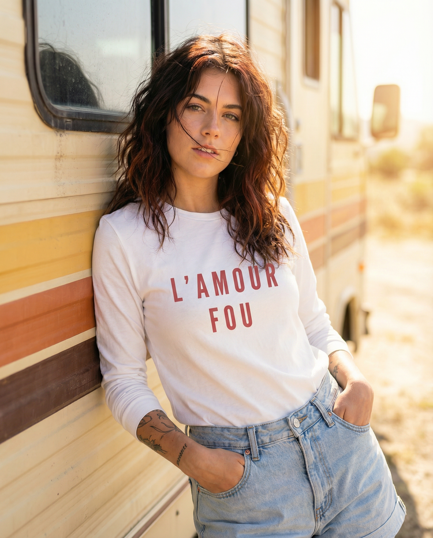 Woman wearing a white sweatshirt with 'L'AMOUR FOU' text, standing next to a vintage-style vehicle.