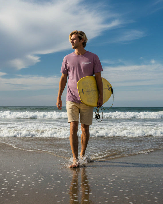 Man walking on a beach with a surfboard under a blue sky with clouds