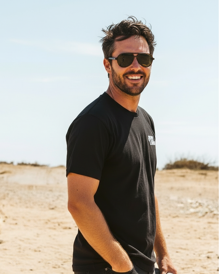 Man wearing sunglasses and a black t-shirt standing in a desert landscape