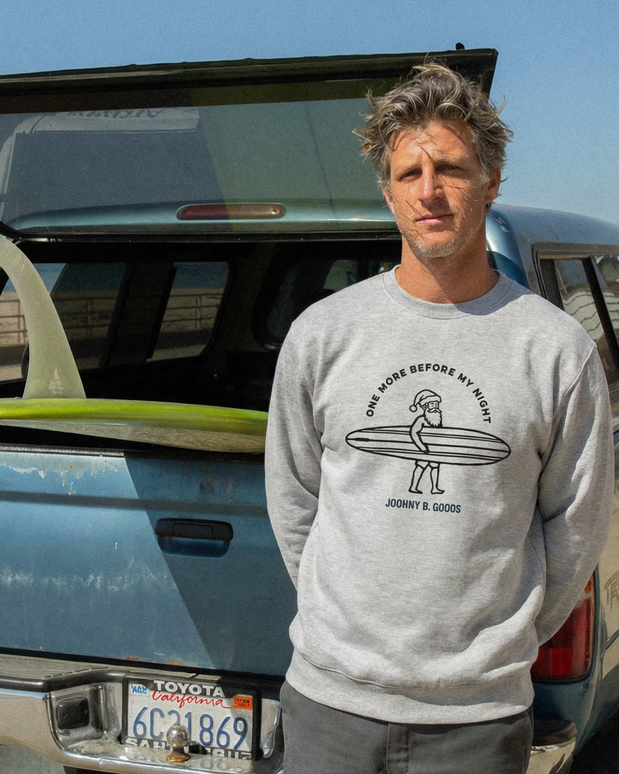 Man standing next to a truck with an open trunk, holding a surfboard.