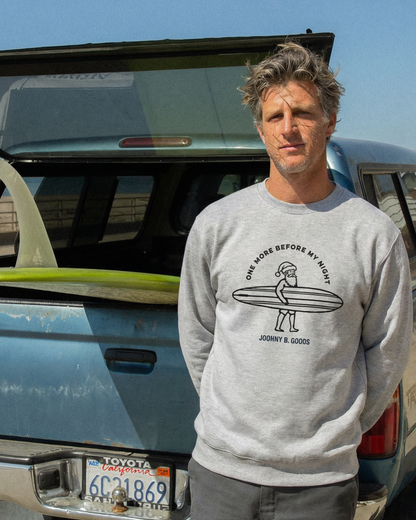 Man standing next to a truck with an open trunk, holding a surfboard.