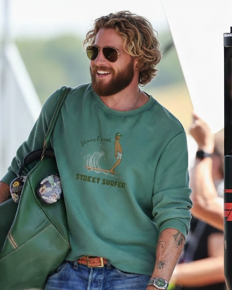 Man wearing a green sweatshirt with a graphic design, holding a green bag, and smiling.
