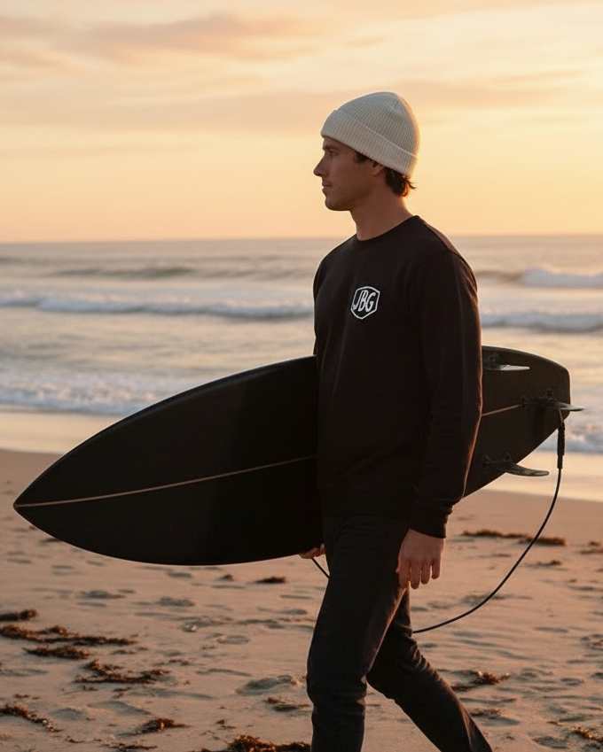 Person walking on a beach with a surfboard at sunset