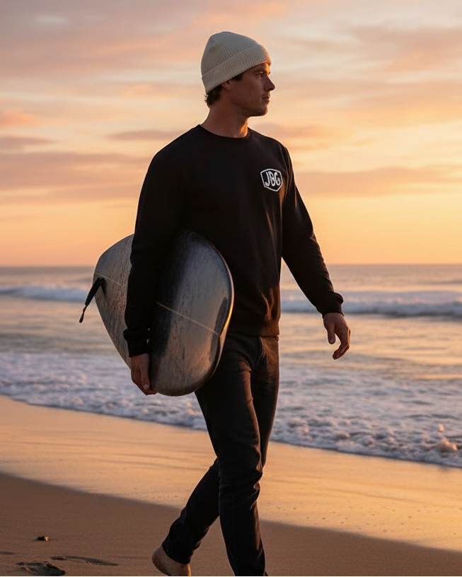 Person in a wetsuit holding a surfboard on a beach at sunset