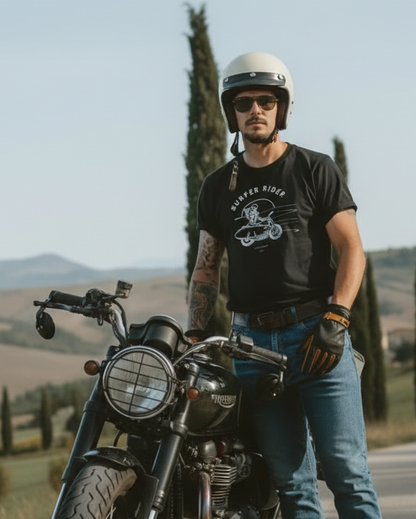 Man with a helmet and gloves standing next to a motorcycle on a scenic road.