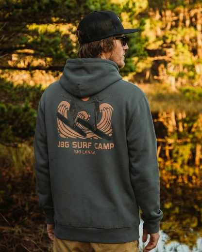 Person wearing a hoodie with a surf camp logo in a forest setting