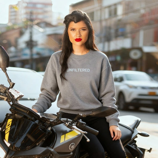 Woman wearing a gray sweatshirt with 'UNFILTERED' text, sitting on a motorcycle in an urban setting.