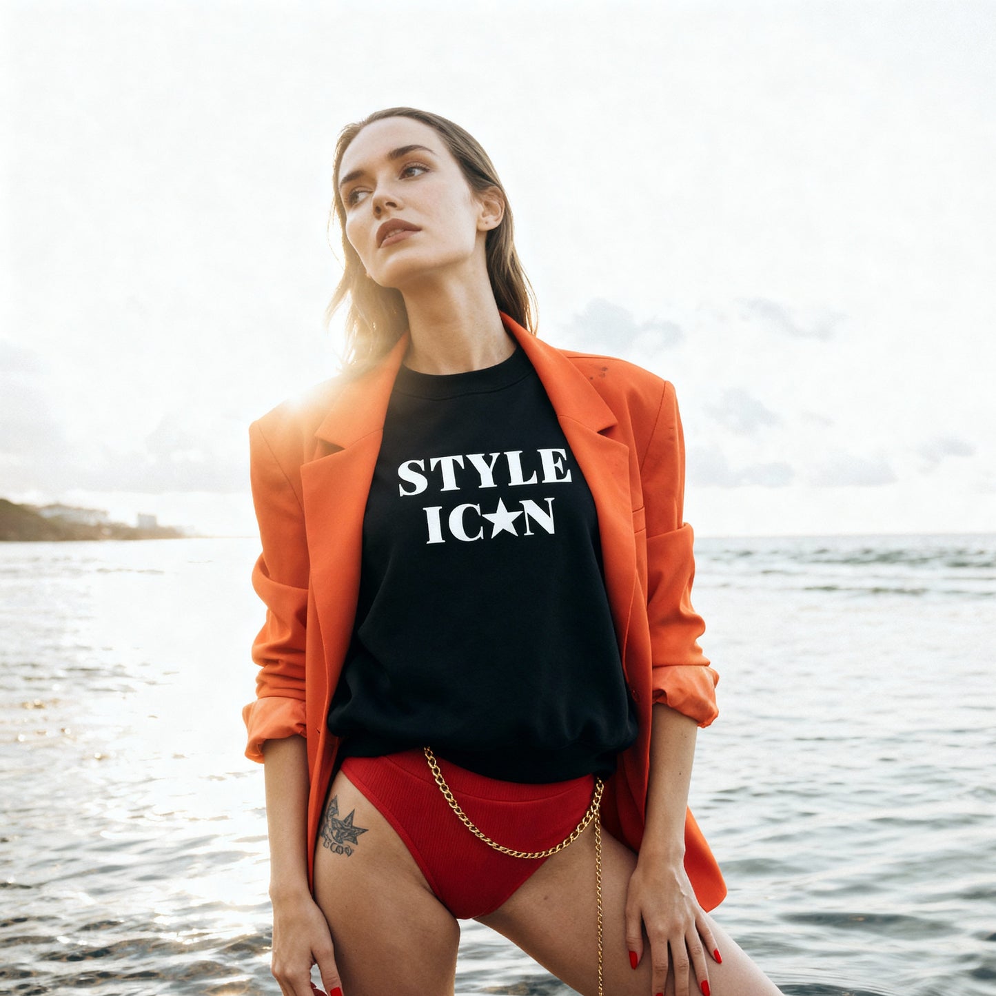 Woman wearing an orange blazer, black JBG  Embroiderd sweatshirt with 'STYLE ICON' text, and red shorts standing in water.
