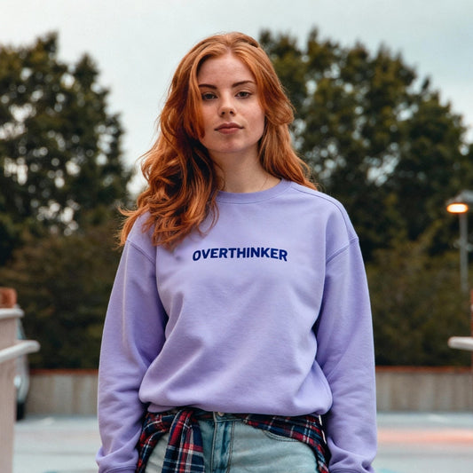 Young Woman wearing a purple Embroidered JBG Brand sweatshirt with 'OVER THINKER' text, standing outdoors.