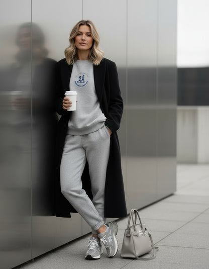 Woman in gray sweatshirt and pants with a coffee cup and handbag in an urban setting