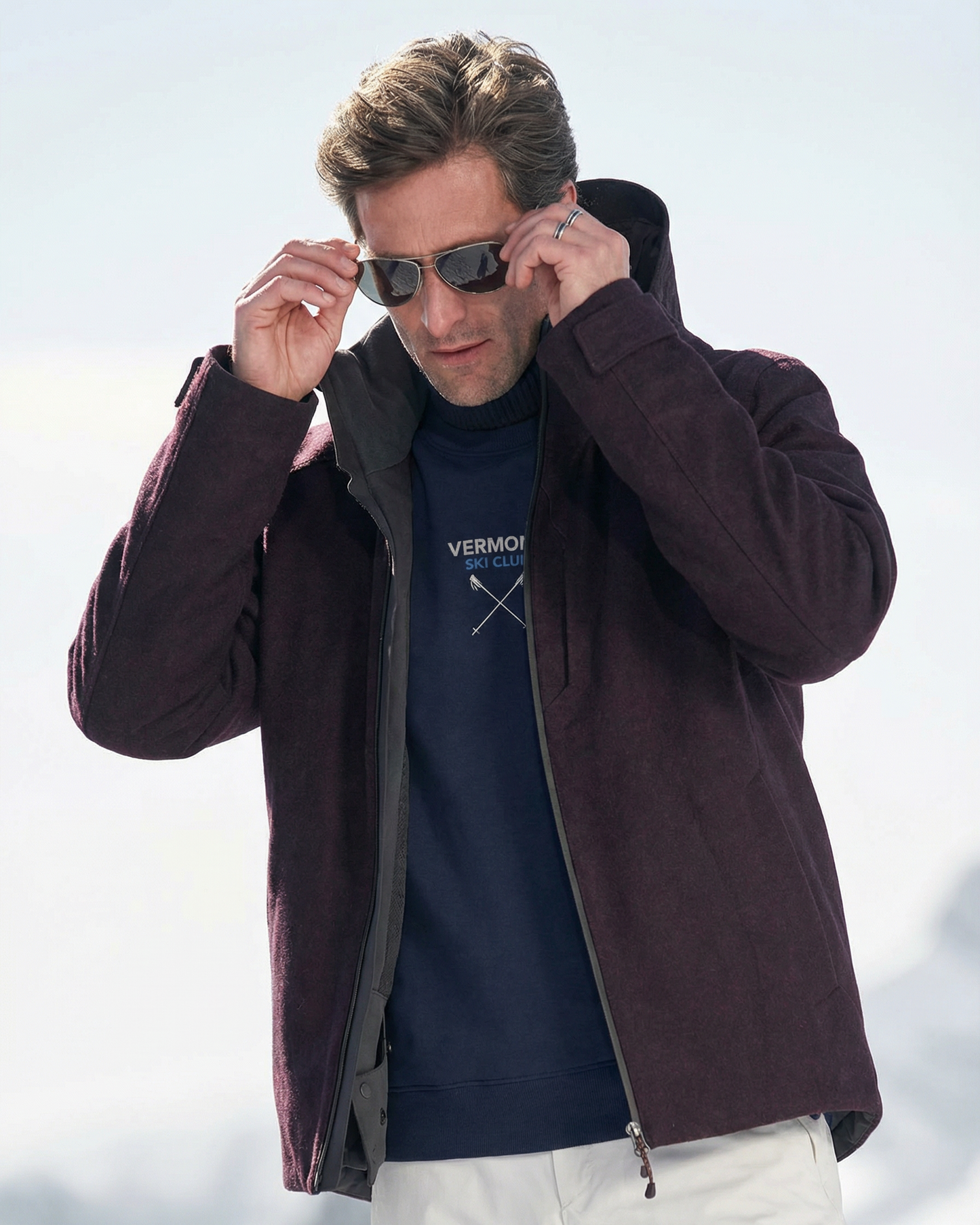 Man wearing a dark brown jacket and sunglasses with a blue shirt in a snowy landscape