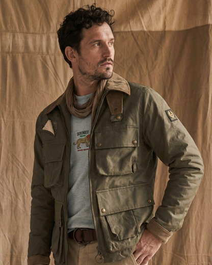 Man wearing a green jacket over a graphic t-shirt against a beige background