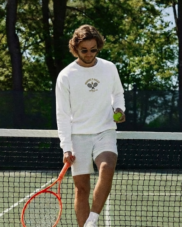 Person on a tennis court holding a racket and a tennis ball, with trees in the background.