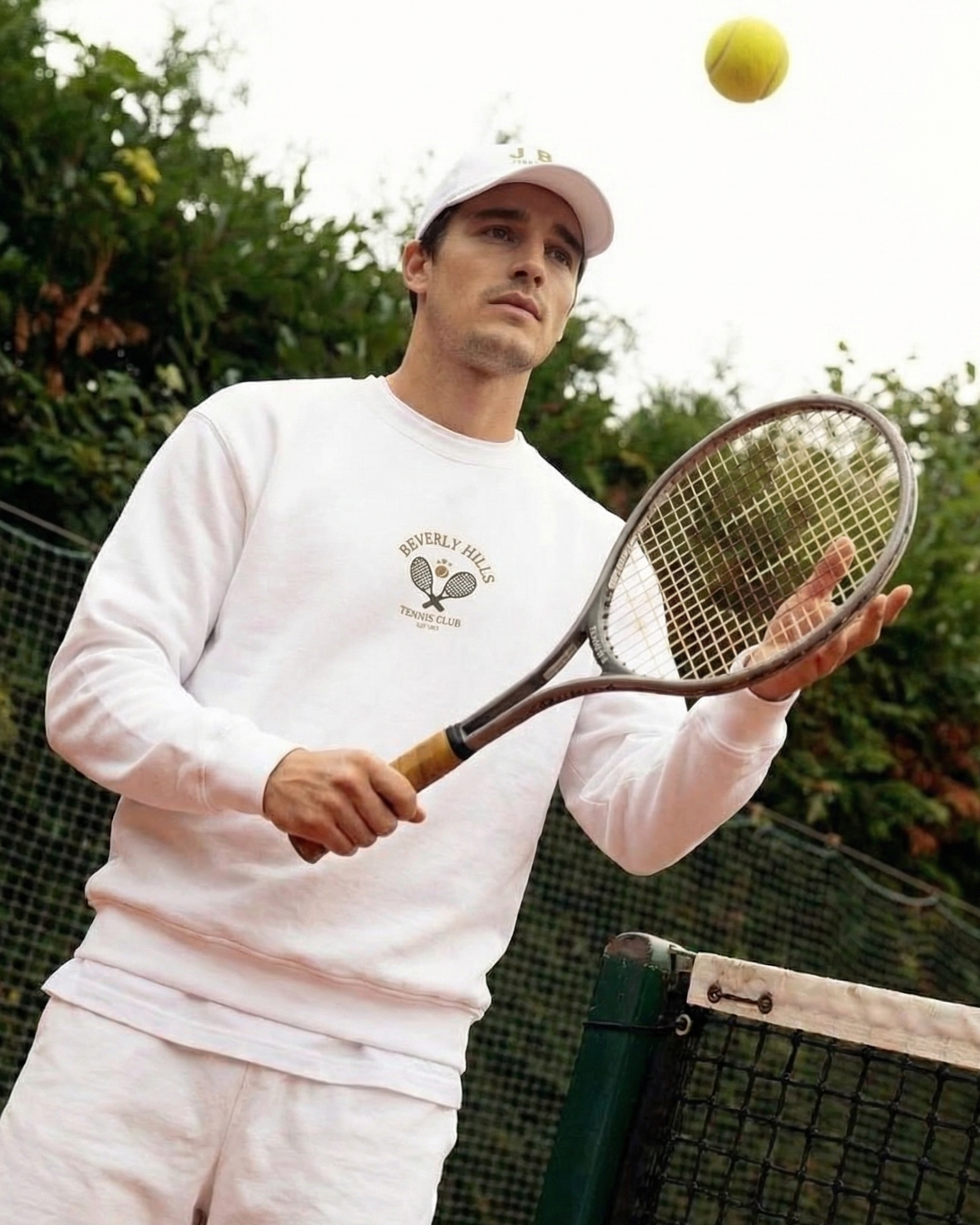 Man in white outfit with a tennis racket and ball on a tennis court
