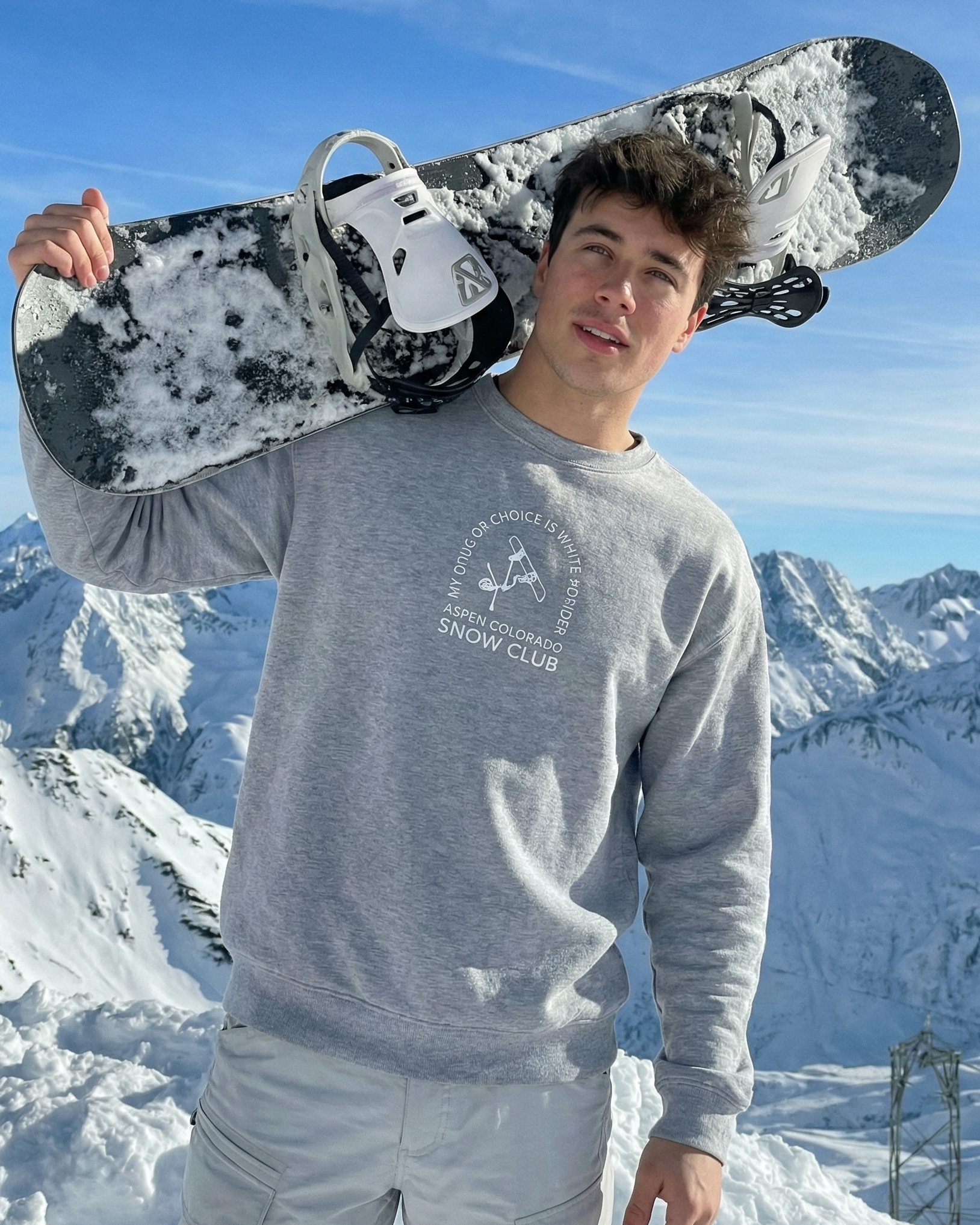 Person holding a snowboard with snowy mountains in the background