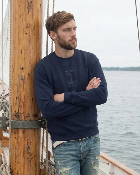 Man standing on a ship's deck with arms crossed, wearing a navy sweater and jeans.