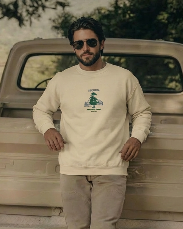 Man wearing a beige sweatshirt with a logo, standing next to an old truck.