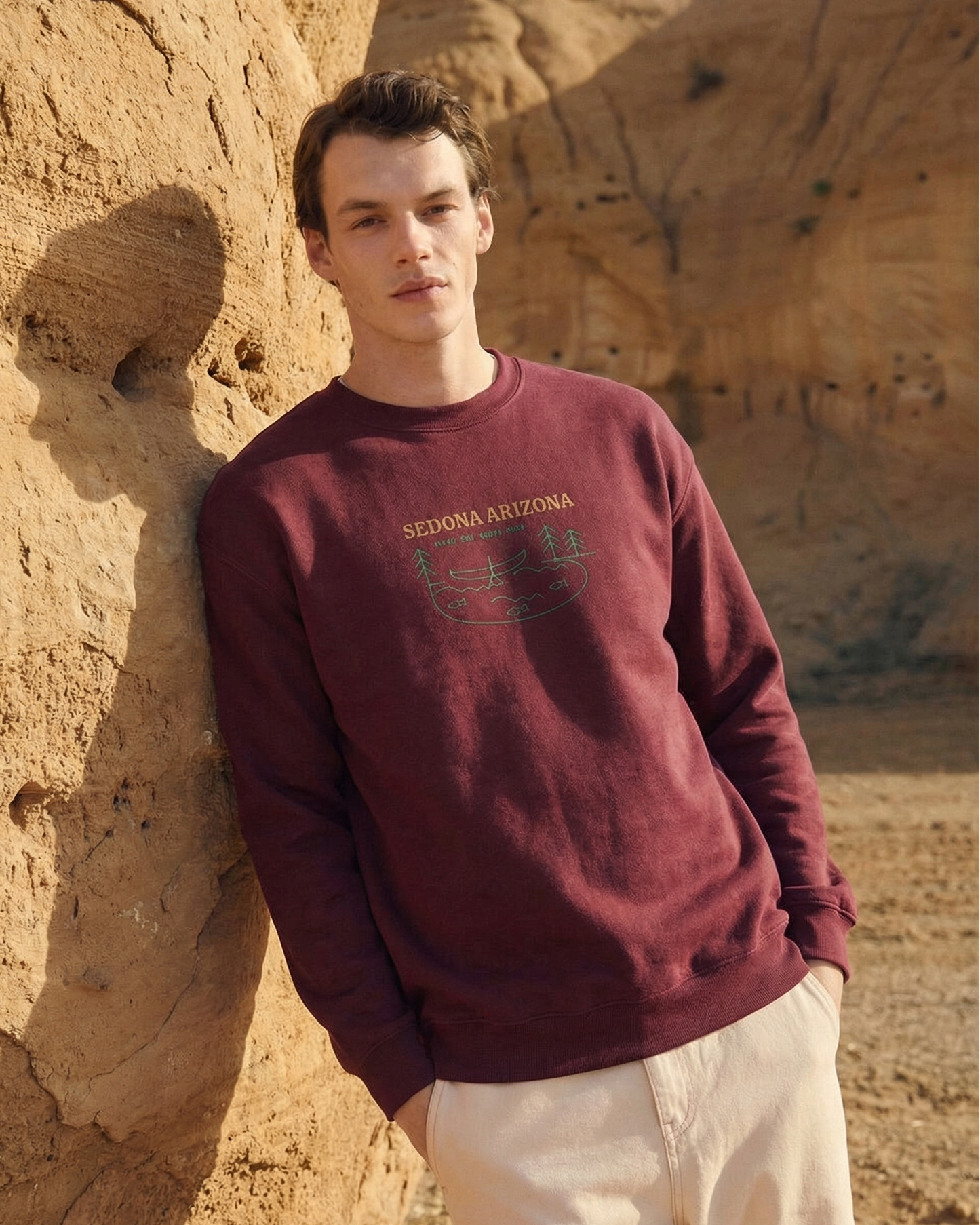 Man wearing a maroon sweatshirt with text, standing against a desert rock formation.