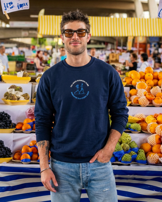 Man wearing sunglasses and a navy sweatshirt with a logo at an outdoor market.