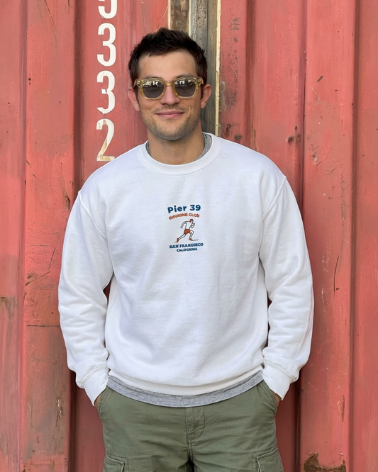 Man wearing a white sweatshirt with text and graphics, standing in front of a red metal door.