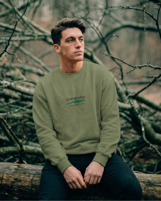 Man sitting on a log in a forest wearing a green sweatshirt with text.