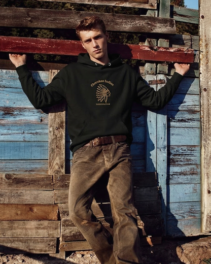 Man wearing a dark hoodie with a logo, standing against a rustic wooden background.