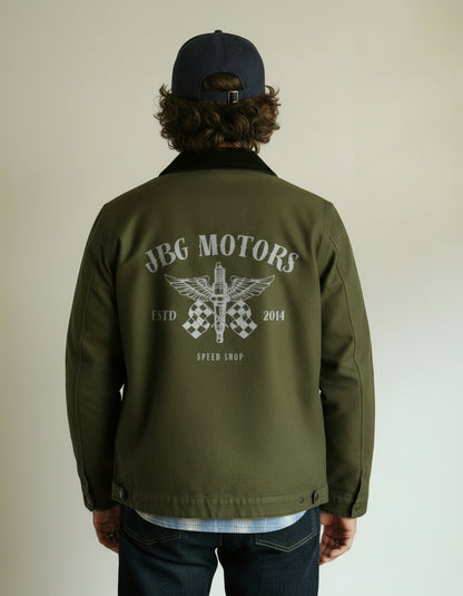 Person wearing an olive green jacket with 'JBG Motors' logo on the back against a plain background