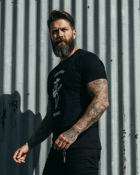Man wearing a black t-shirt and pants standing against a corrugated metal wall.