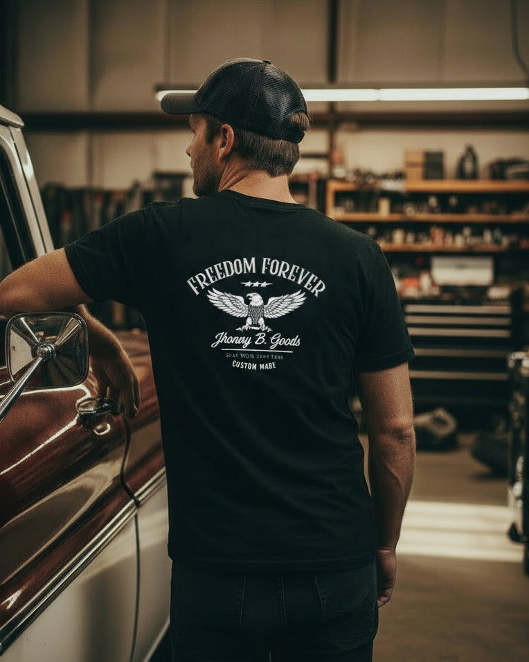 Man wearing a black t-shirt with 'Freedom Forever' text, standing next to a vintage car in a garage.