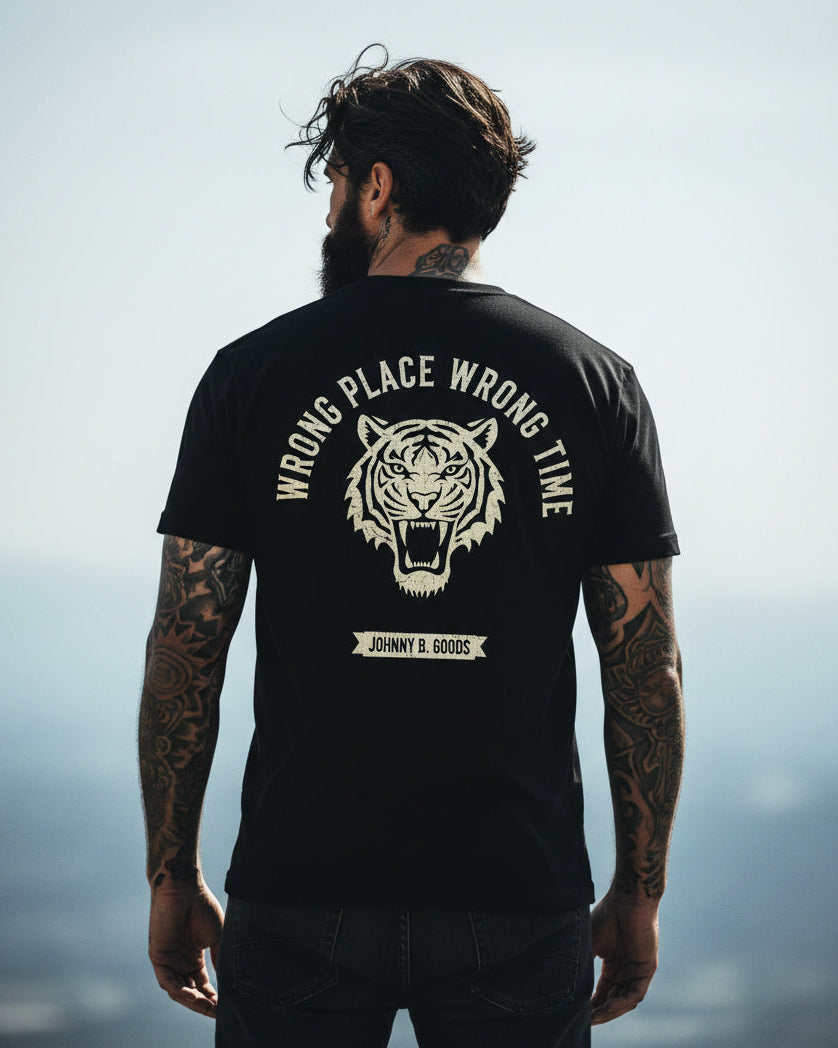 Man wearing a black t-shirt with a tiger graphic and text, standing against a blurred natural background.