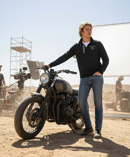 Man standing next to a motorcycle in a desert setting with filming equipment in the background