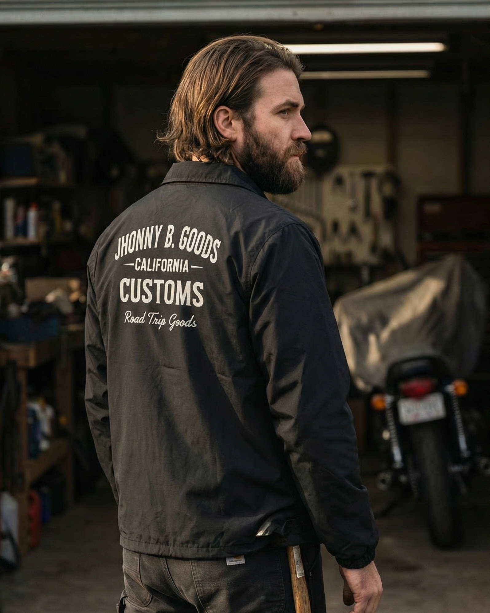 Man wearing a black jacket with 'Honny B. Goods Customs' branding in a garage setting.