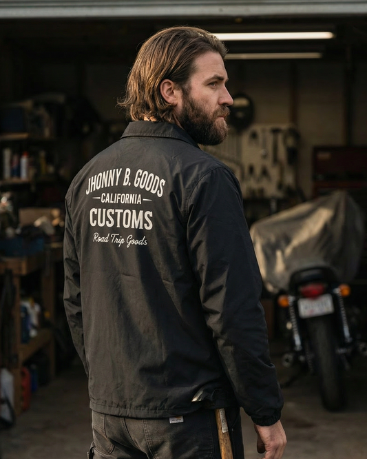 Man wearing a black jacket with 'Honny B. Goods Customs' branding in a garage setting.