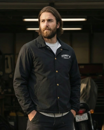 Man wearing a dark jacket with a logo in a garage setting
