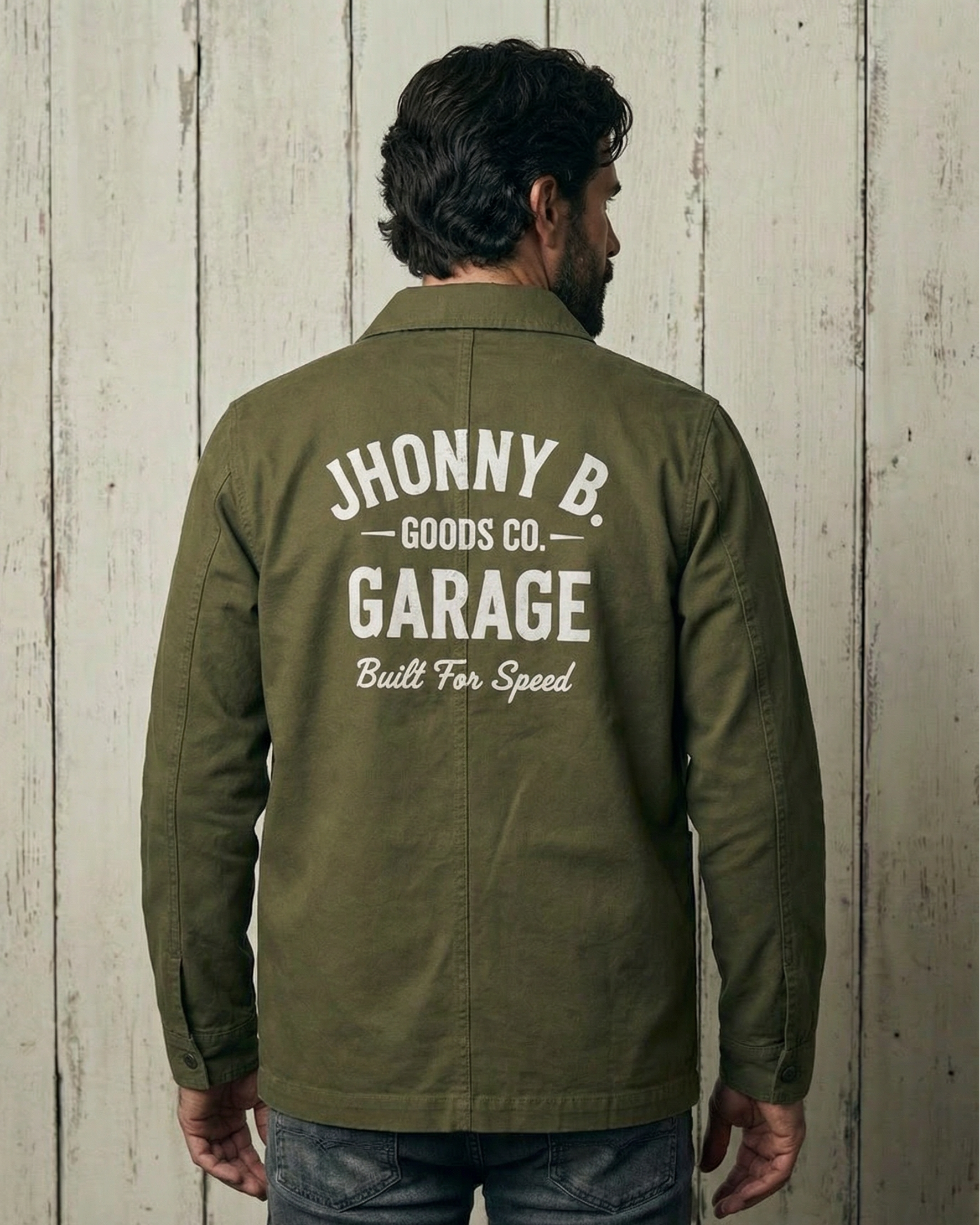 Person wearing a green jacket with 'Jhonny B. Goods Co. Garage' text on the back against a wooden wall.