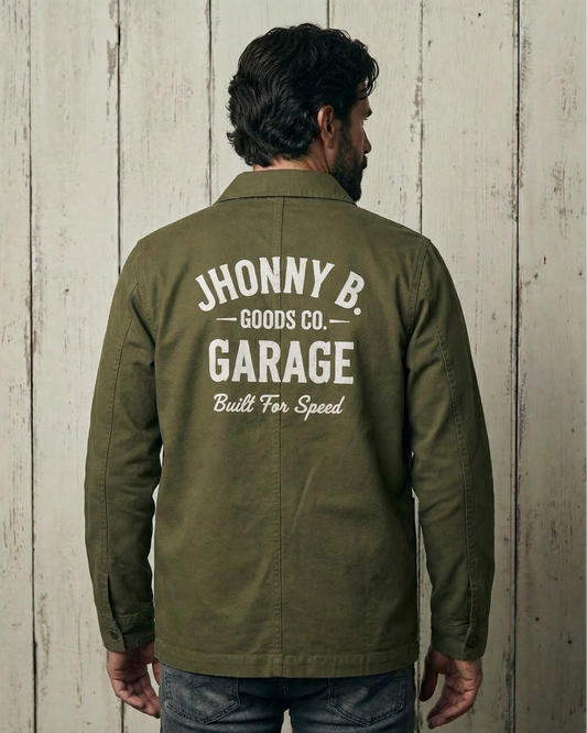 Person wearing a green jacket with 'Jhonny B. Goods Co. Garage' text on the back against a wooden wall.