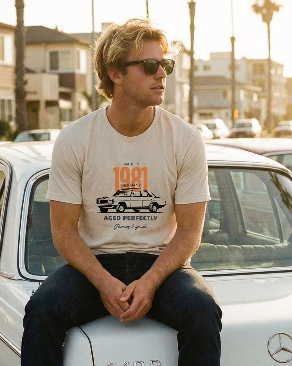 Person sitting on a vintage Mercedes-Benz car with palm trees and buildings in the background