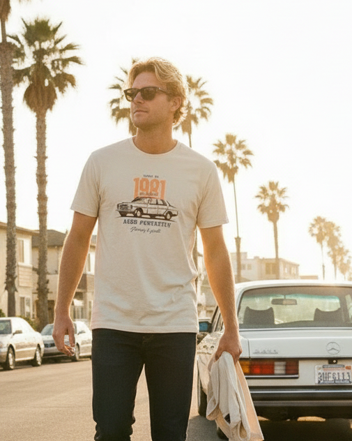 Man wearing a white t-shirt with a graphic design, standing on a street with palm trees in the background.