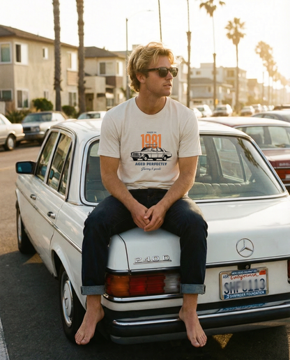 Man sitting on a white Mercedes-Benz car with palm trees and buildings in the background