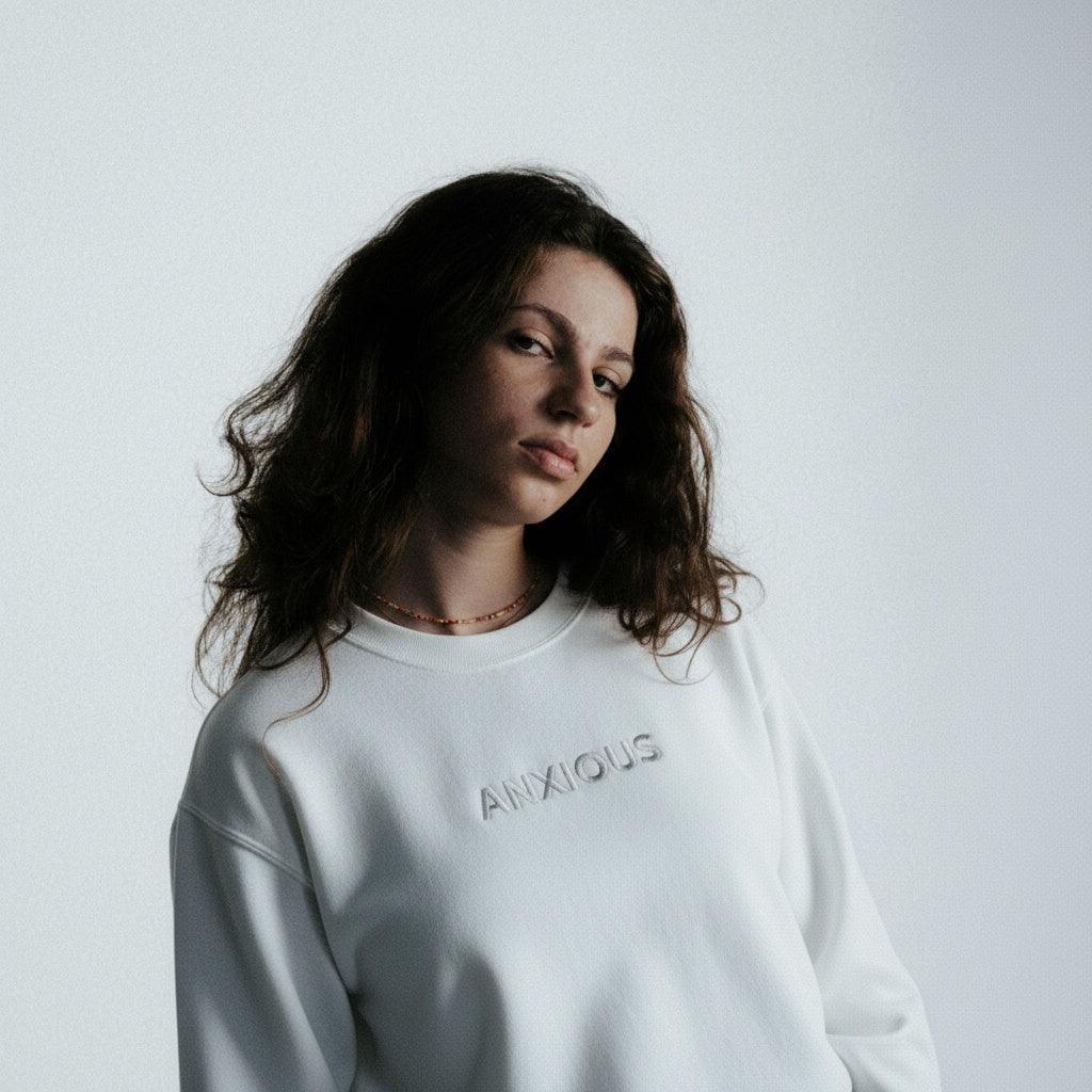 Person wearing a white sweatshirt with 'ANXIOUS' text on a plain background