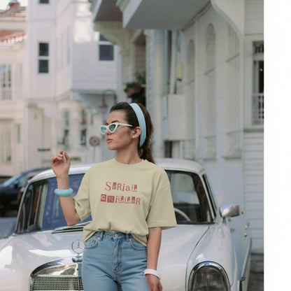 Woman wearing a t-shirt with text, standing in front of a vintage car on a street.